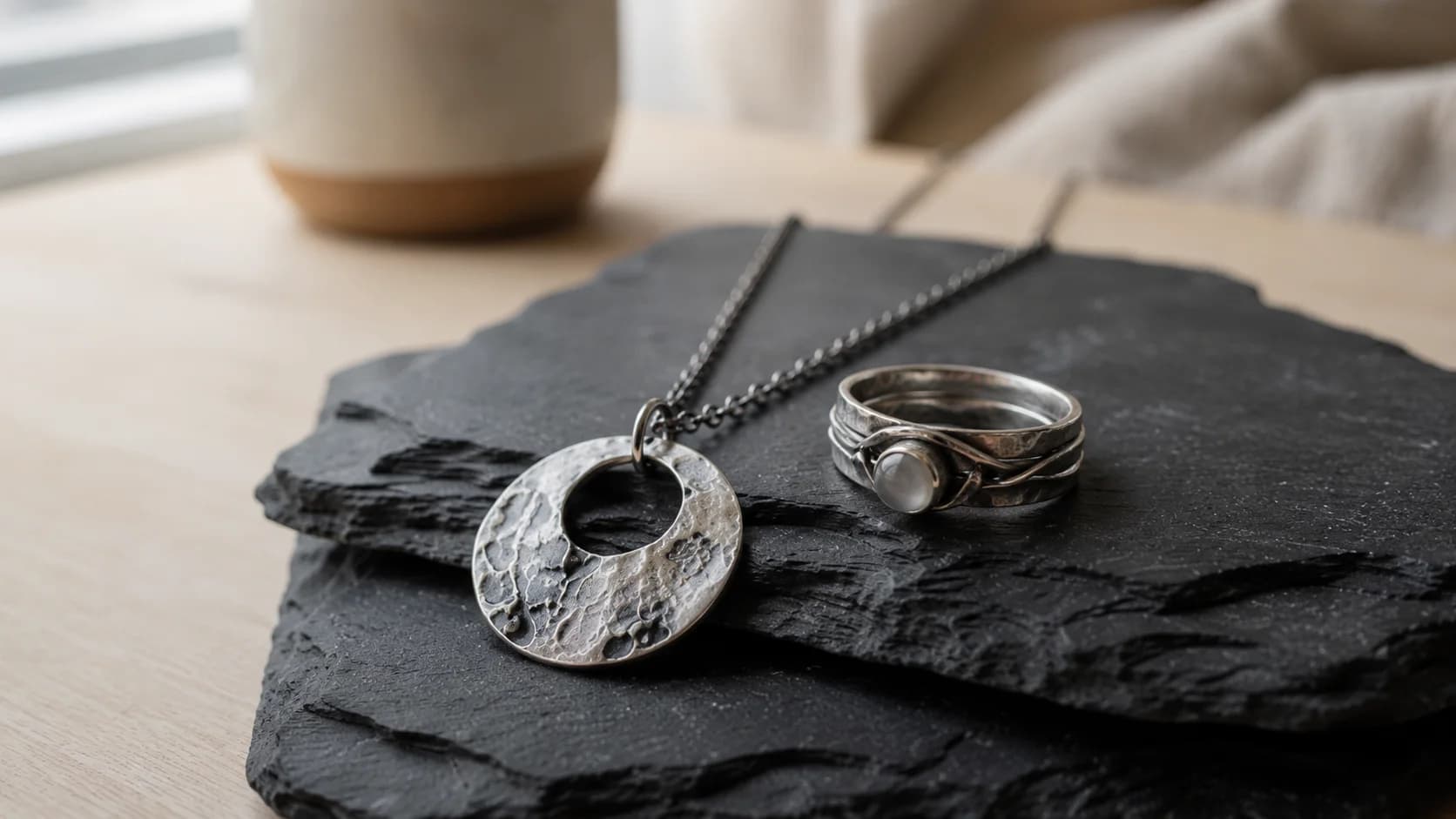 Handmade silver pendant necklace and ring resting on a dark slate stone