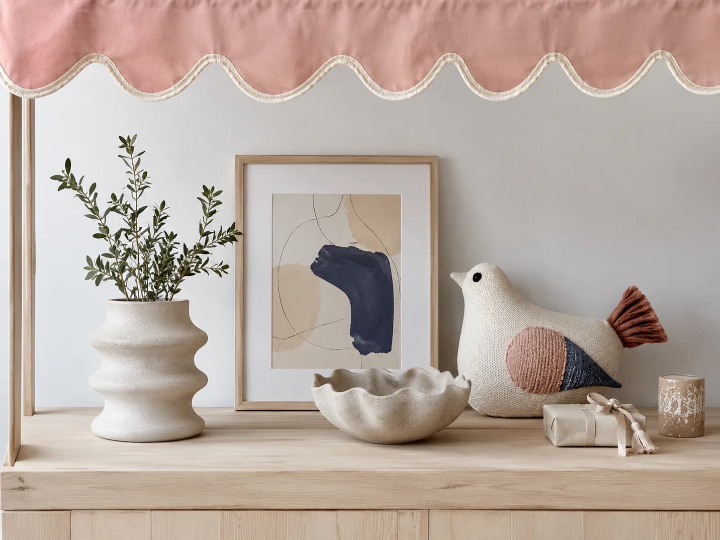 Styled shelf with a cream ceramic vase, sprig of greenery, framed art and a ceramic bird ornament