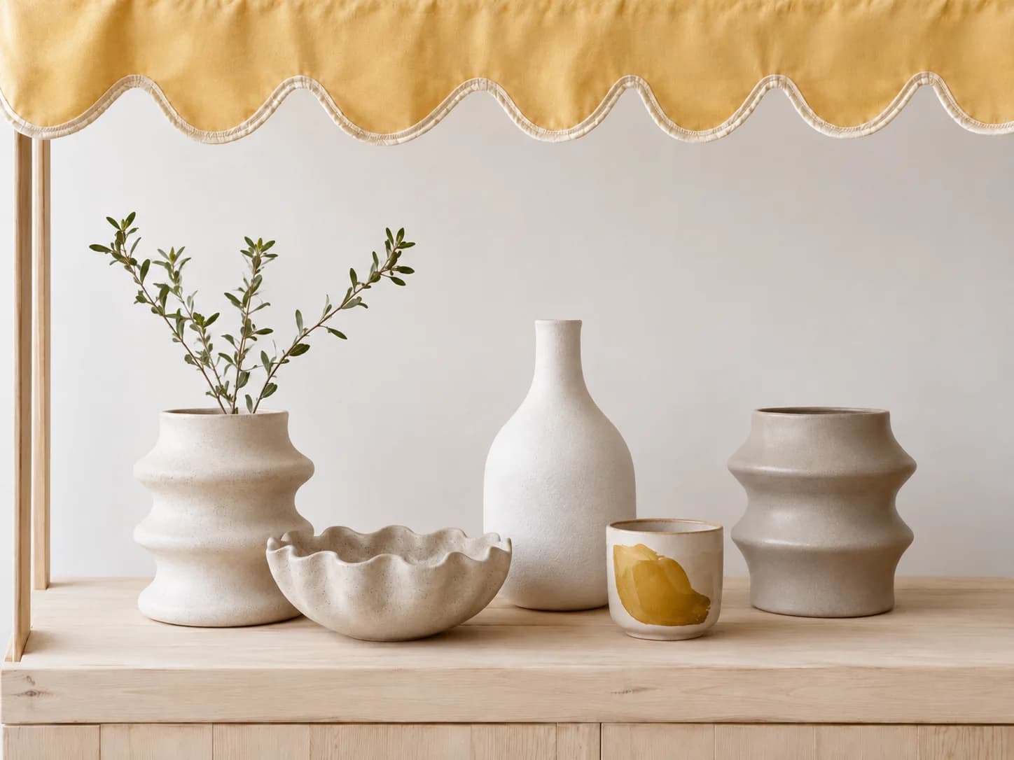 Cream ceramic vases and bowls with a sprig of greenery on a shelf